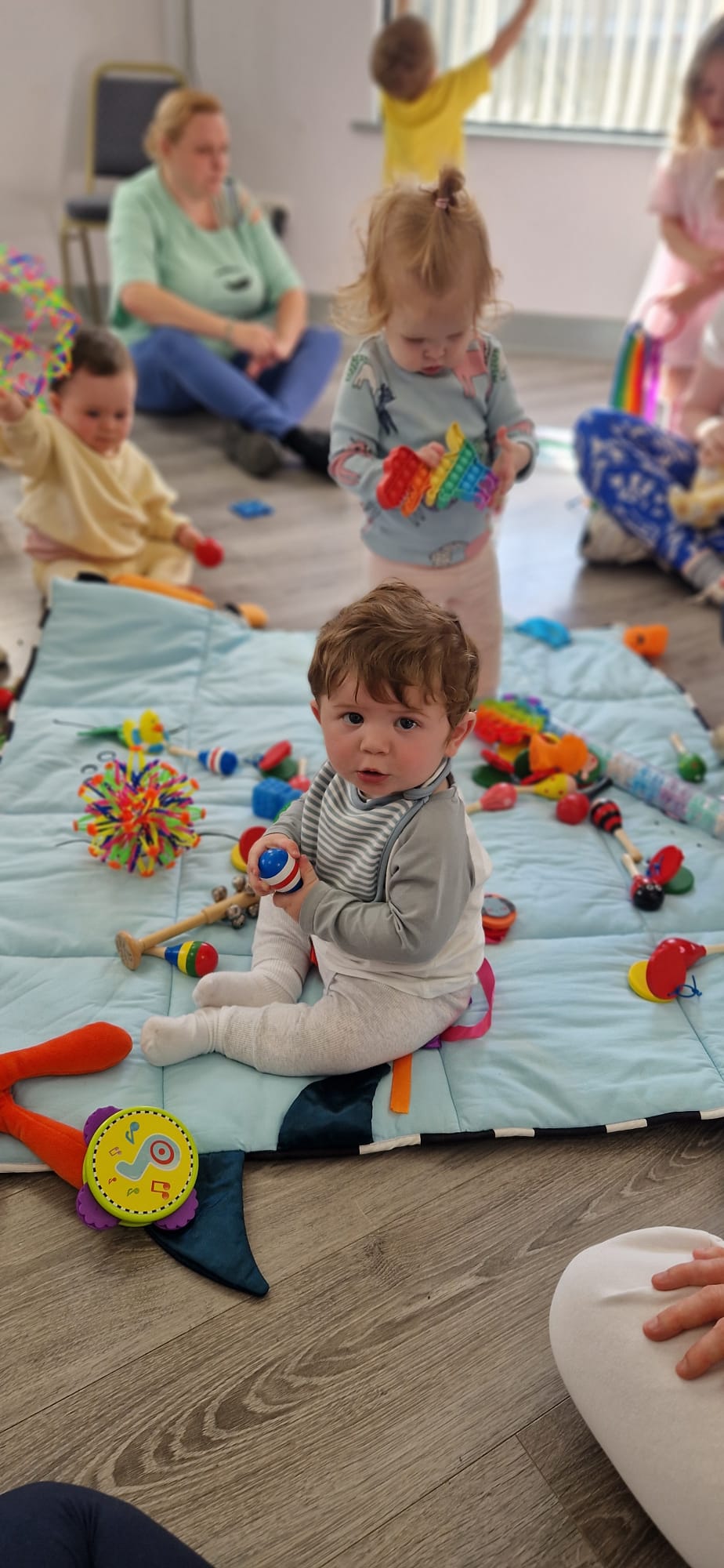 Two little ones playing with instruments on a blue mat at Zumbini class